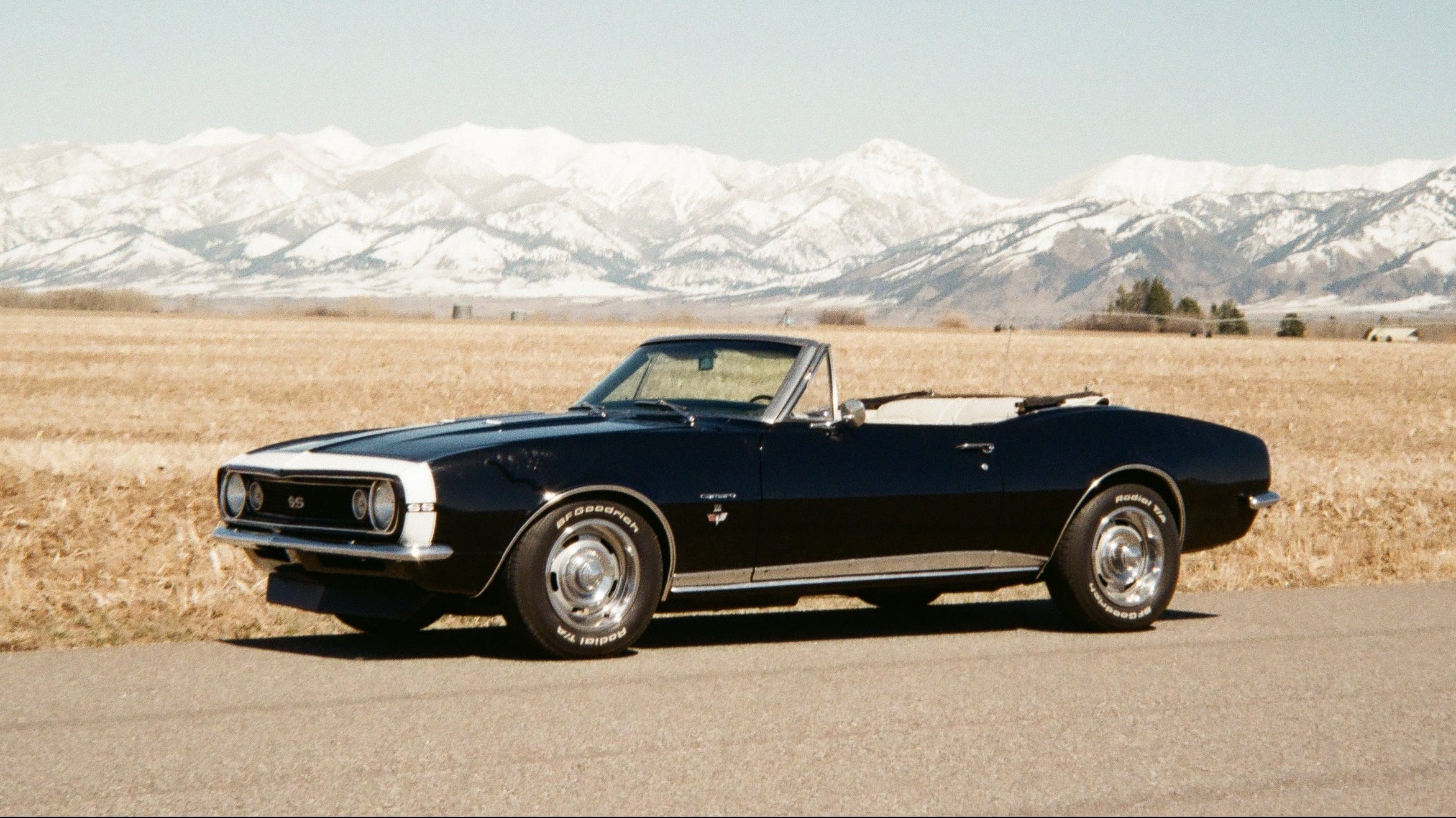 Black convertible car on a road with snow-capped mountains in the background