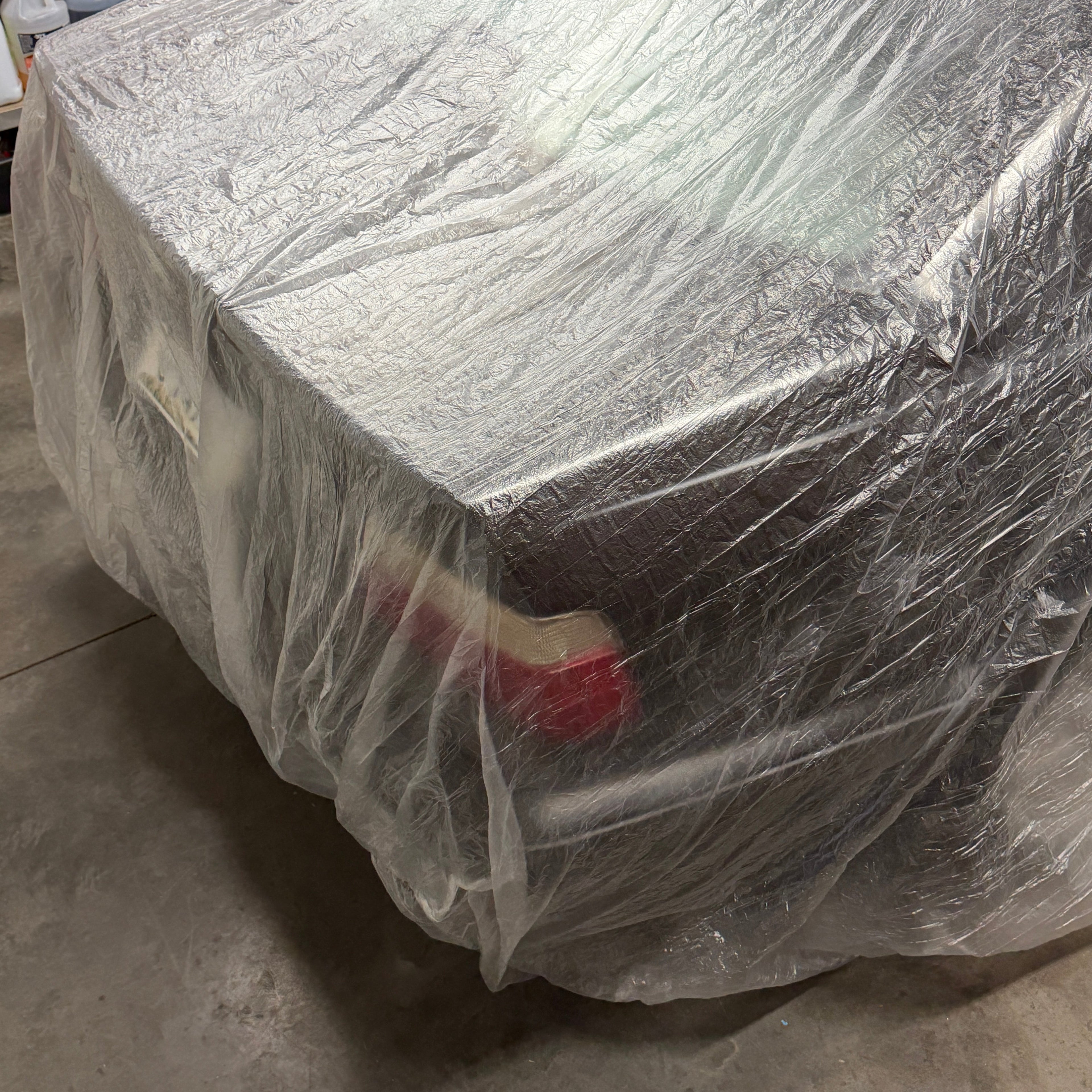 BMW E36 wrapped in plastic on a concrete garage floor